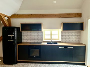 Rovná kuchyňská linka dlouhá 5,2 metru s masivní dubovou pracovní deskou o síle 38 mm, ošetřenou voskovým olejem OSMO pro zátěžové plochy a kontakt s potravinami. Dvířka a čela zásuvek dýhovaná LTD dub, ošetřena barvou Tikkurila - symphony - antracit. Výklopný systém horních dvířek Blum Aventos, který je společně se zásuvkami řešen bezúchytkovým systémem otevírání ''push to open''. Díky tomu bylo možné zachovat kompaktní linie a plochy, které jsou pro tento design charakteristické.