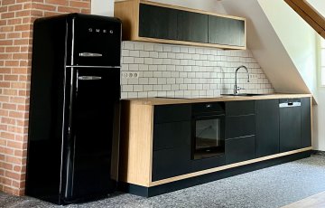 Rovná kuchyňská linka dlouhá 5,2 metru s masivní dubovou pracovní deskou o síle 38 mm, ošetřenou voskovým olejem OSMO pro zátěžové plochy a kontakt s potravinami. Dvířka a čela zásuvek dýhovaná LTD dub, ošetřena barvou Tikkurila - symphony - antracit. Výklopný systém horních dvířek Blum Aventos, který je společně se zásuvkami řešen bezúchytkovým systémem otevírání ''push to open''. Díky tomu bylo možné zachovat kompaktní linie a plochy, které jsou pro tento design charakteristické.